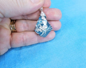 May include: A silver wire wrapped pendant featuring a light blue gemstone. The wire is shaped into a floral design.