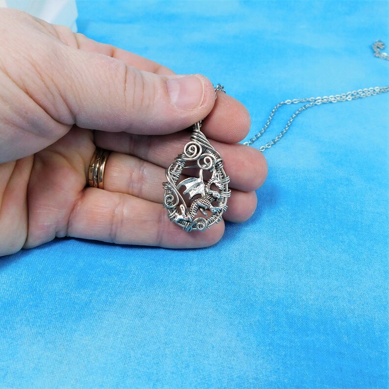 May include: A silver wire-wrapped pendant featuring a dragon design. The pendant is hanging from a silver chain.