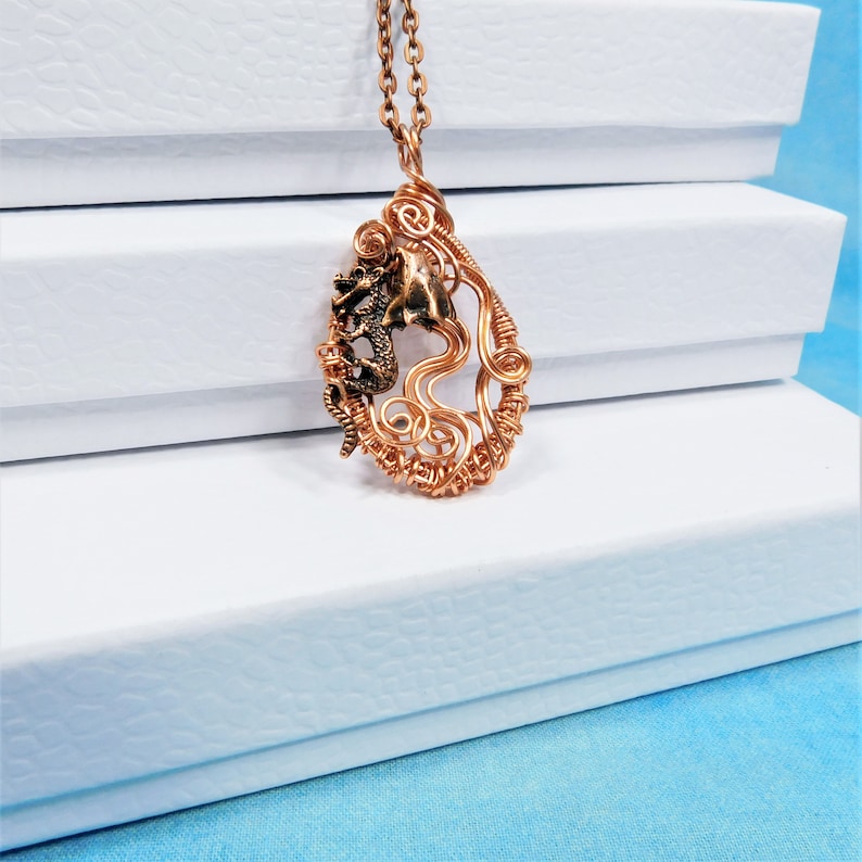 May include: A copper wire wrapped pendant necklace featuring a dragon design. The pendant is shaped like a teardrop and has a detailed dragon figure in the center.