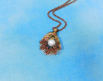 May include: A pendant necklace featuring a single white spherical bead encased in a complex, swirling cage of dark copper-toned wire. The pendant is suspended from a matching copper-colored metal chain with small, uniform oval links.