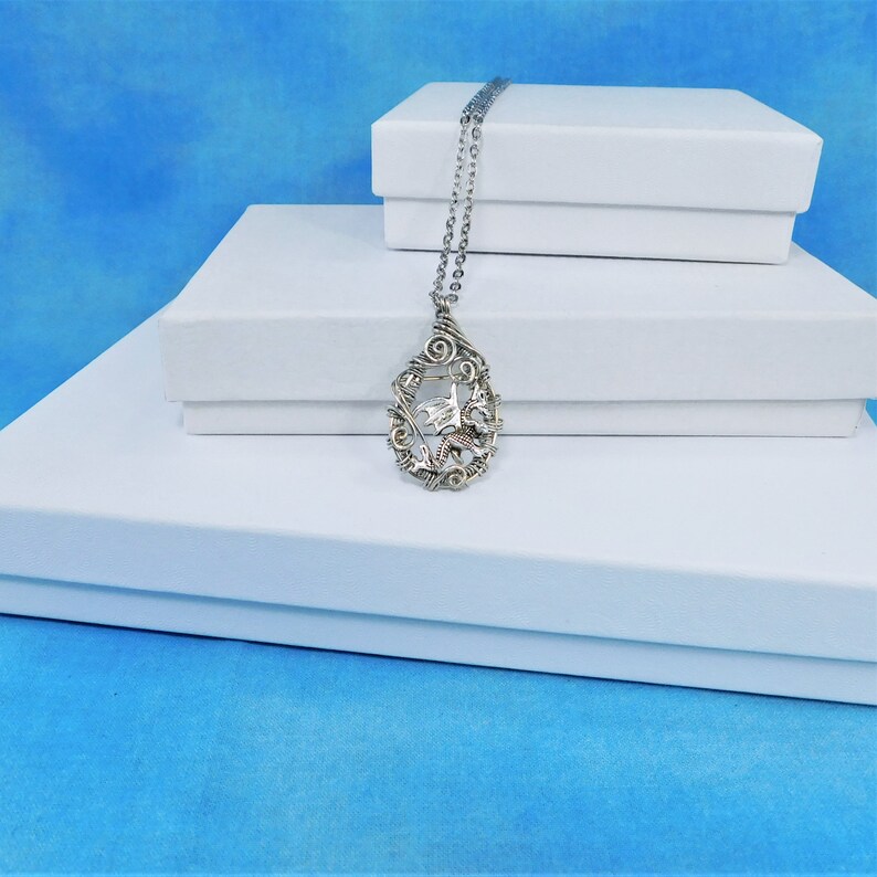 May include: A silver chain necklace with a silver and gold pendant featuring a dragon design. The necklace is displayed on top of three white boxes.