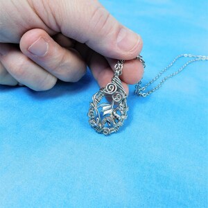May include: A silver wire-wrapped pendant necklace featuring a dragon design. The pendant is oval-shaped and hangs from a silver chain.
