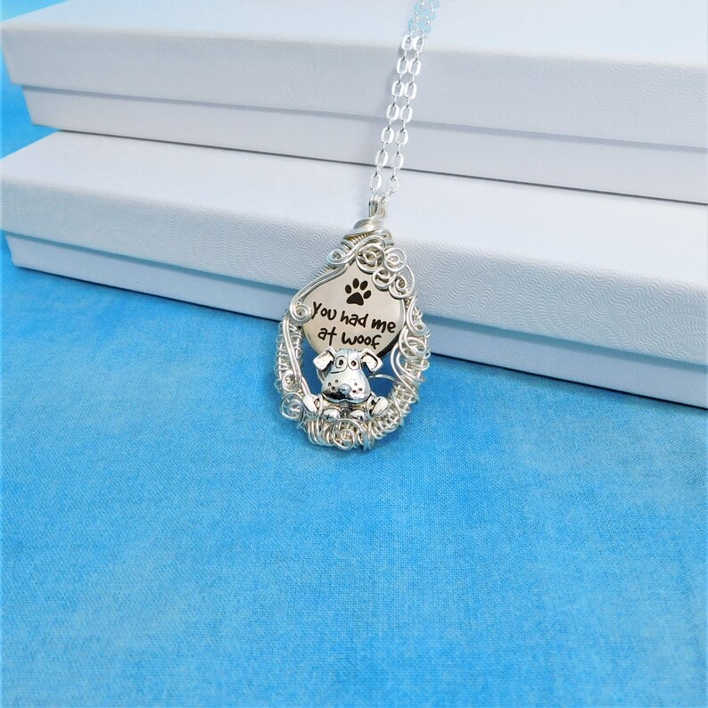 May include: Silver necklace with a wire-wrapped pendant featuring a dog silhouette and the text "You had me at woof".