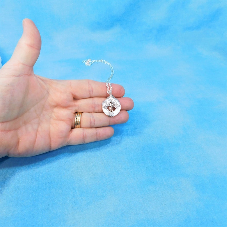 May include: A silver necklace with a round pendant featuring a wire-wrapped tree design.