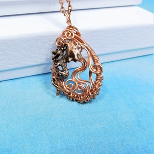 May include: A copper wire wrapped pendant featuring a small dragon figurine. The pendant is shaped like a teardrop and has a delicate, intricate design.
