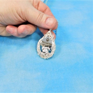 May include: Silver necklace with a teardrop-shaped pendant. The pendant is wire-wrapped and features a small dog silhouette and the inscription "You had me at woof".