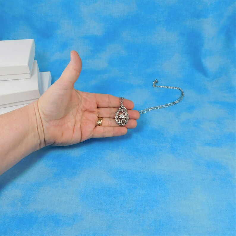 May include: A silver pendant necklace with a delicate, openwork design featuring a bird in flight. The pendant is hanging from a silver chain.