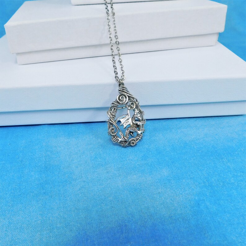 May include: A silver necklace with a wire-wrapped pendant featuring a dragon design.