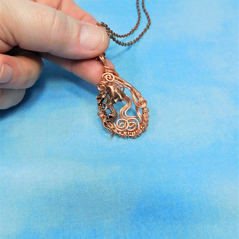 May include: A copper wire wrapped pendant necklace featuring a stylized dragon design. The pendant is shaped like a teardrop and has a detailed wirework design.