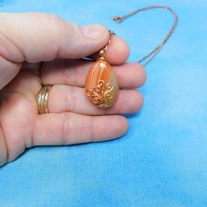 May include: A copper wire wrapped agate pendant with a tree design. The pendant is on a copper chain and is being held in a hand.