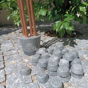 Könnte beinhalten: Ein Kupferrohr mit einem grauen Betonfuß und einem weißen Sternmuster. Das Rohr ist von einem Haufen grauer Granitsteine umgeben.