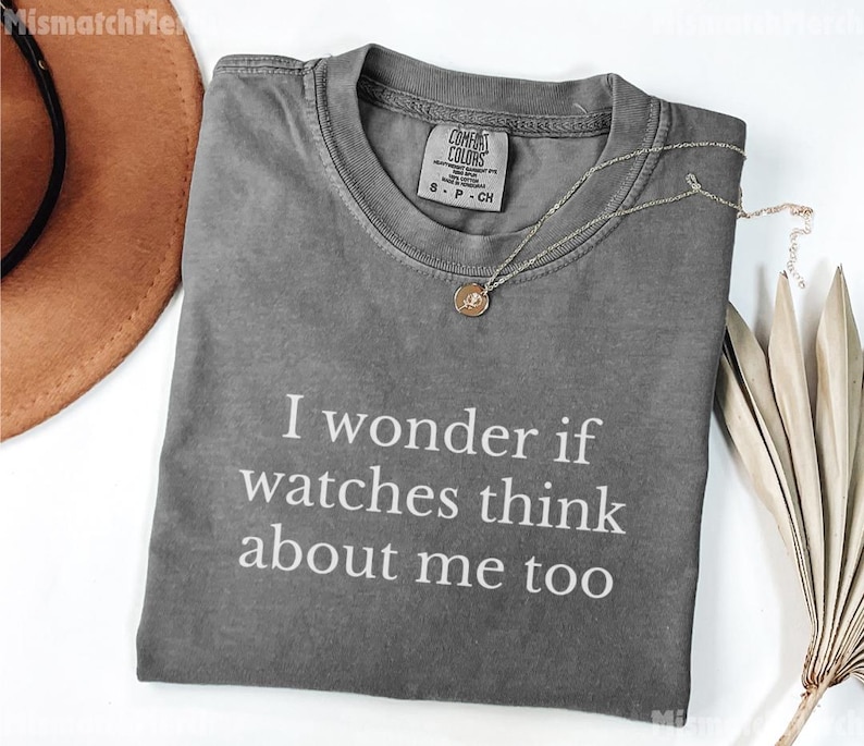 May include: A gray Comfort Colors t-shirt with the text "I wonder if watches think about me too" in white. A silver necklace with a small pendant is on the shirt.