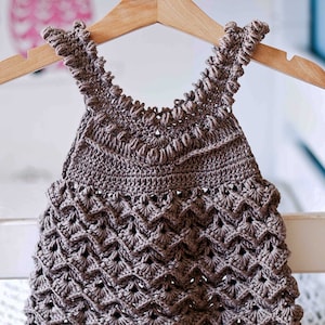 May include: A brown crocheted baby dress with a scalloped hem and a delicate lace pattern.