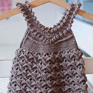 May include: A brown crocheted baby dress with a scalloped hem and a delicate floral pattern.