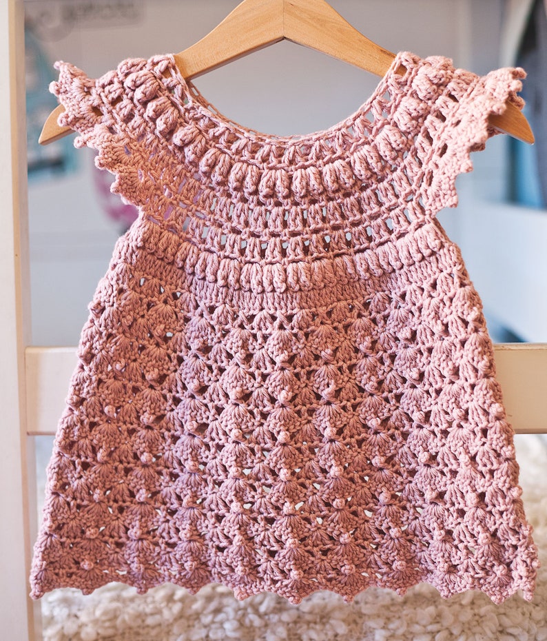 Peut inclure: Une robe de b&eacute;b&eacute; en crochet rose avec un ourlet festonn&eacute; et des manches bouffantes.