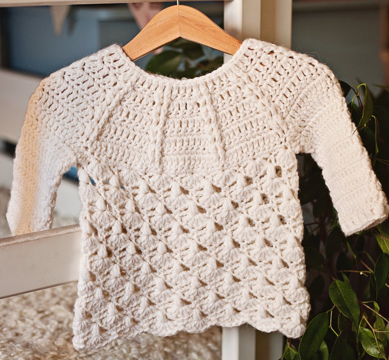May include: A white crocheted sweater with a delicate, lacy pattern. The sweater has a round neckline and long sleeves.