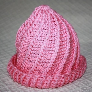 May include: A pink knitted hat with a cable knit pattern. The hat is made of soft yarn and has a simple design.