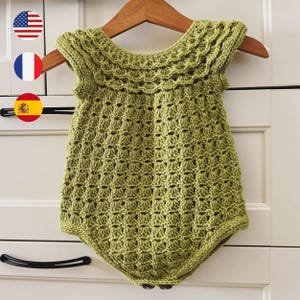 May include: A light olive green sleeveless romper featuring a textured crochet stitch pattern throughout the body. The garment has a scalloped edge detail around the neckline and armholes, with a rounded bottom hem and visible buttons at the base.