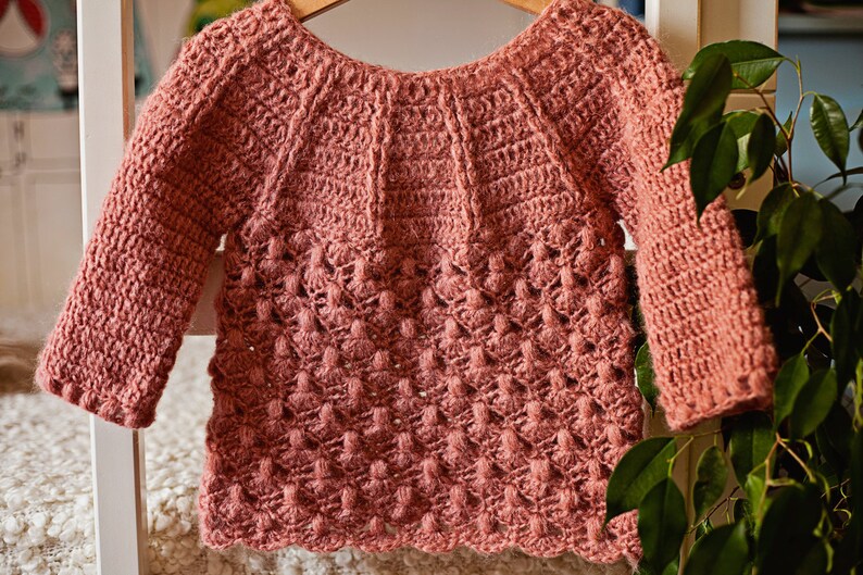 May include: A pink crocheted sweater with a textured stitch pattern and long sleeves.