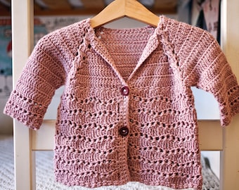 Op de afbeelding: Een roze gebreide cardigan met knoopsluiting en een V-hals. De cardigan heeft een delicaat opengewerkt patroon.