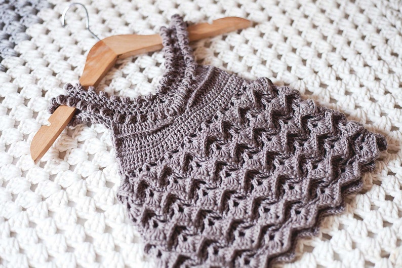 May include: A crocheted sleeveless top in a light brown colour with a delicate stitch pattern. The top is hanging on a wooden hanger.