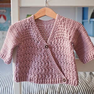 May include: A pink crocheted cardigan with a button closure. The cardigan has a V-neck and is made with a textured stitch.
