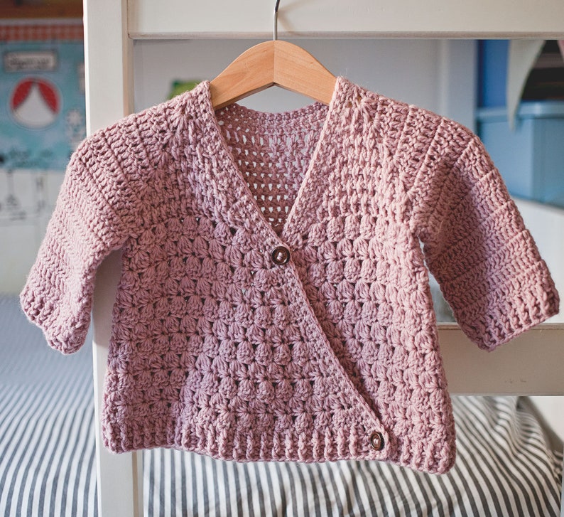 May include: A pink crocheted cardigan with a button closure. The cardigan has a V-neck and is made with a textured stitch.