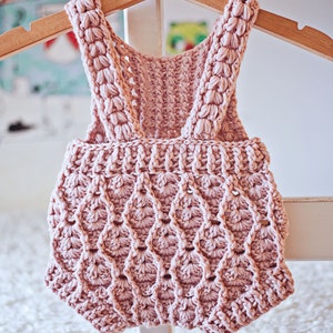Op de afbeelding: Een roze gebreide baby romper met een gegolfd ontwerp. De romper heeft bandjes die aan de schouders vastgebonden worden.