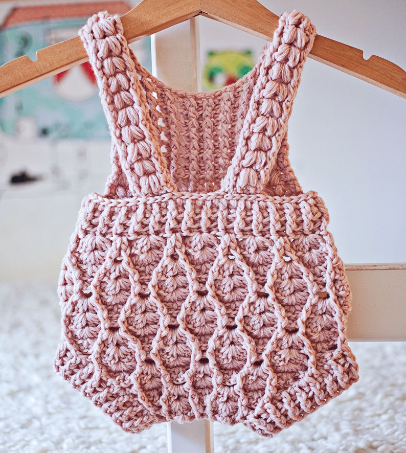 Op de afbeelding: Een roze gebreide baby romper met een gegolfd ontwerp. De romper heeft bandjes die aan de schouders vastgebonden worden.