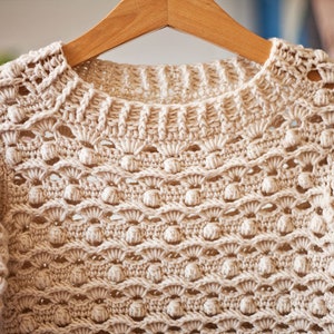 May include: A beige crocheted sweater with a delicate openwork pattern and a round neckline.