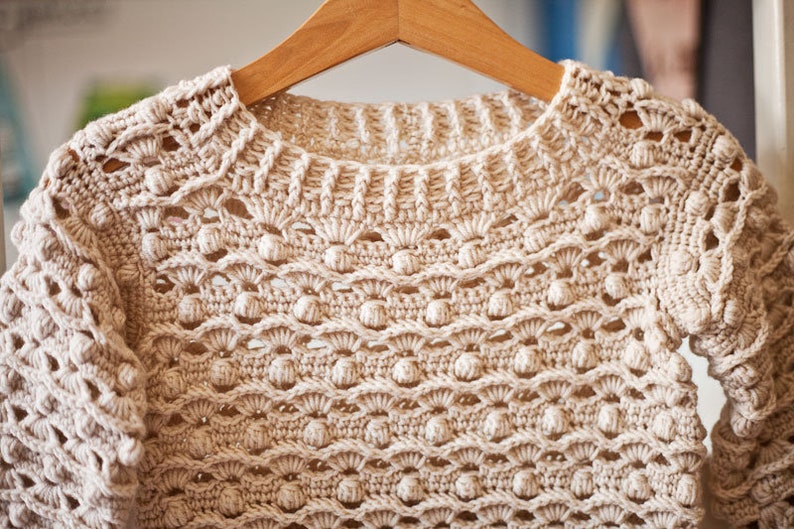 May include: A beige crocheted sweater with a delicate openwork pattern and a round neckline.