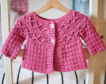 May include: A pink crocheted cardigan with a button closure and a lacy design around the neckline and sleeves.