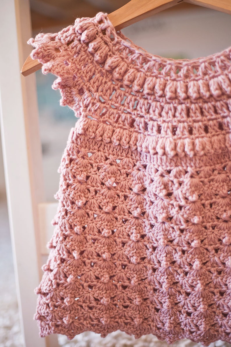 Peut inclure: Une robe de b&eacute;b&eacute; en crochet rose avec un design d&eacute;licat et ajour&eacute; et un ourlet festonn&eacute;.