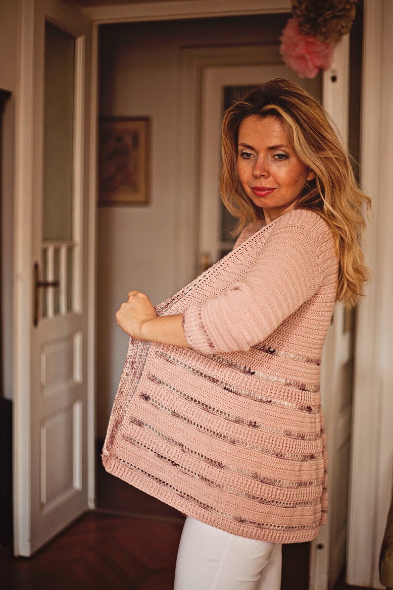 Peut inclure: Un cardigan en crochet rose avec un motif ray&eacute;. Le cardigan est ouvert &agrave; l'avant et a des manches longues.