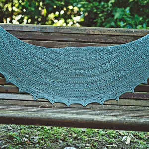 May include: A teal crocheted shawl with a scalloped edge, draped over a wooden bench.