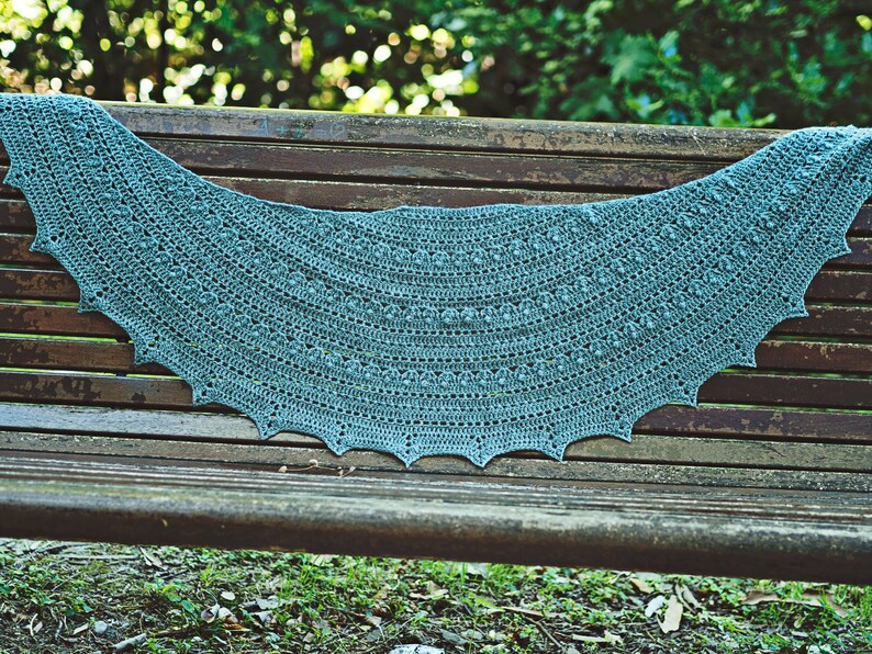 May include: A teal crocheted shawl with a scalloped edge, draped over a wooden bench.