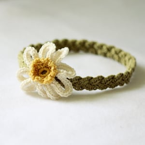 May include: A crocheted headband with a white daisy flower. The headband is green and the flower has a yellow center.