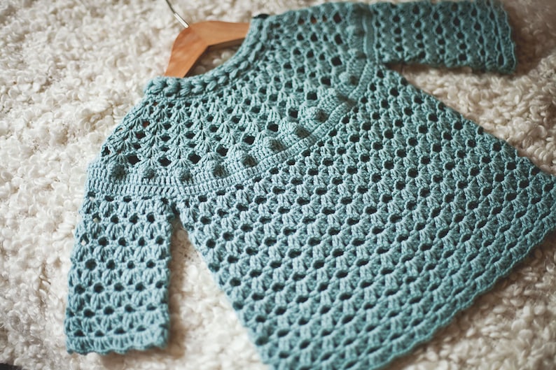 Puede incluir: Un su&eacute;ter de crochet azul claro con un patr&oacute;n delicado. El su&eacute;ter tiene mangas largas y un cuello redondo.