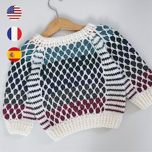 May include: A long-sleeve crochet sweater featuring a white base with a textured bobble stitch pattern in alternating horizontal bands of teal, dark blue, charcoal gray, and deep burgundy, finished with a ribbed white neckline and cuffs.