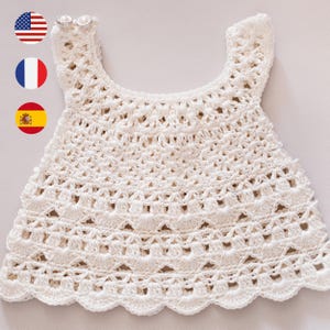 May include: An off-white, hand-crocheted top with a scalloped edge. The top has a delicate openwork pattern and small straps. This item is likely intended for a baby or toddler.