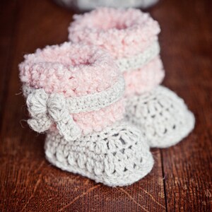 Puede incluir: Un par de botitas de beb&eacute; de crochet en rosa y gris. Las botitas tienen una parte superior de color rosa esponjosa y una suela de crochet gris.