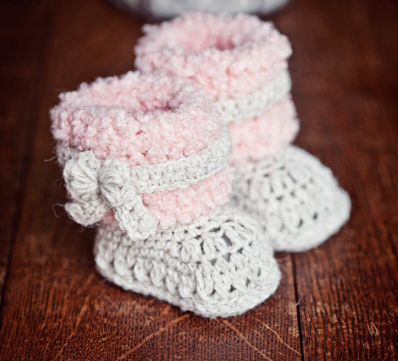 Puede incluir: Un par de botitas de beb&eacute; de crochet en rosa y gris. Las botitas tienen una parte superior de color rosa esponjosa y una suela de crochet gris.