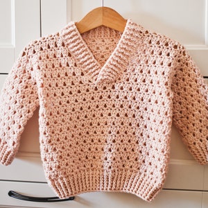 May include: A pink crocheted sweater with a V-neck and long sleeves.