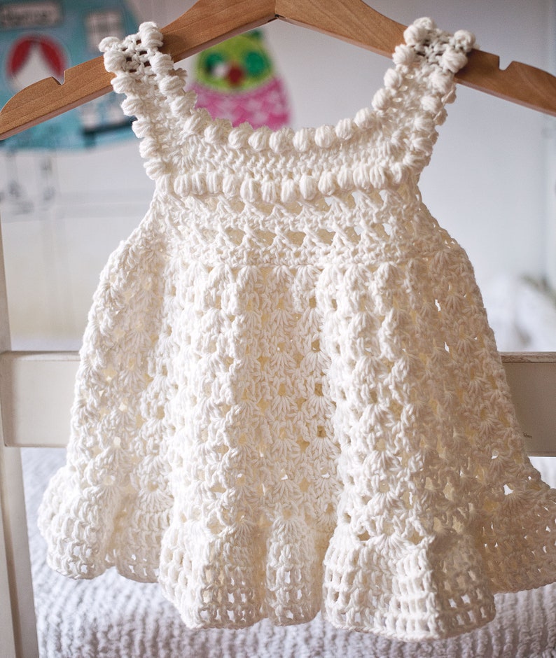 May include: A white crocheted baby dress with a scalloped hem and a beaded neckline.