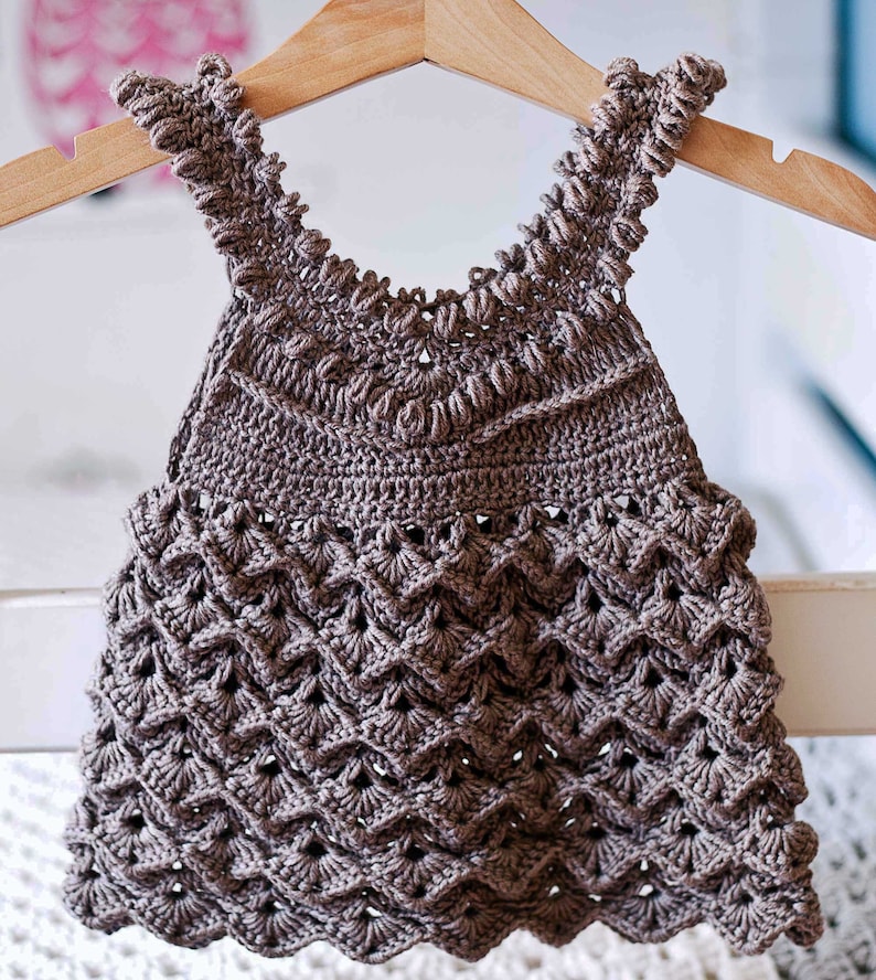 May include: A brown crocheted baby dress with a scalloped hem and a delicate lace pattern.