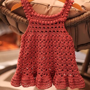 May include: A crocheted baby dress in a deep pink color with a scalloped hem and a delicate lace pattern.