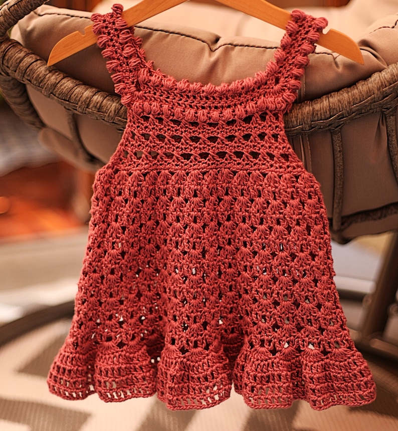 May include: A crocheted baby dress in a deep pink color with a scalloped hem and a delicate lace pattern.