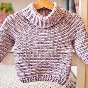 May include: A light purple crocheted sweater with a turtleneck and long sleeves.