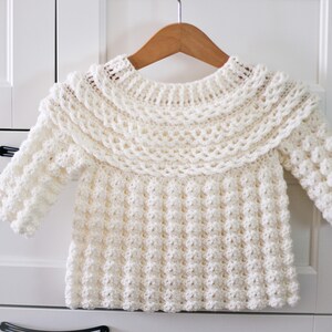 K&ouml;nnte beinhalten: Ein wei&szlig;er H&auml;kelpullover mit einem R&uuml;schenkragen und einem strukturierten Stichmuster.