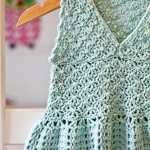 May include: A light blue crocheted sleeveless top with a scalloped hem and a V-neck.